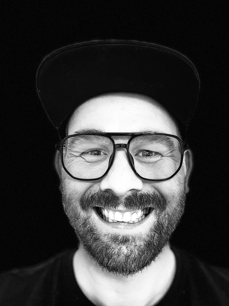 Manuel Fuß, lachend, mit Brille und schwarzer Kappe